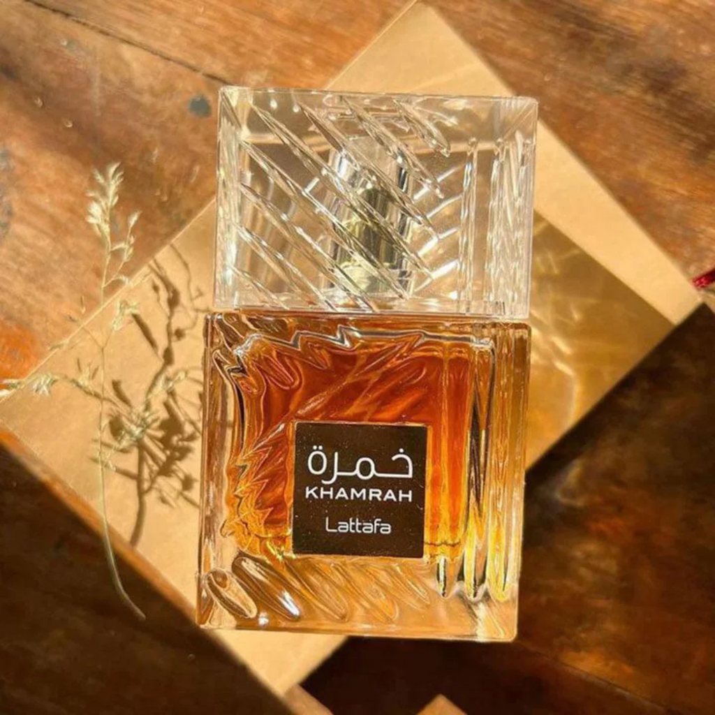 Lattafa Khamrah perfume bottle with rich amber liquid placed on warm wooden surface with sunlight shadows creating a luxury aesthetic