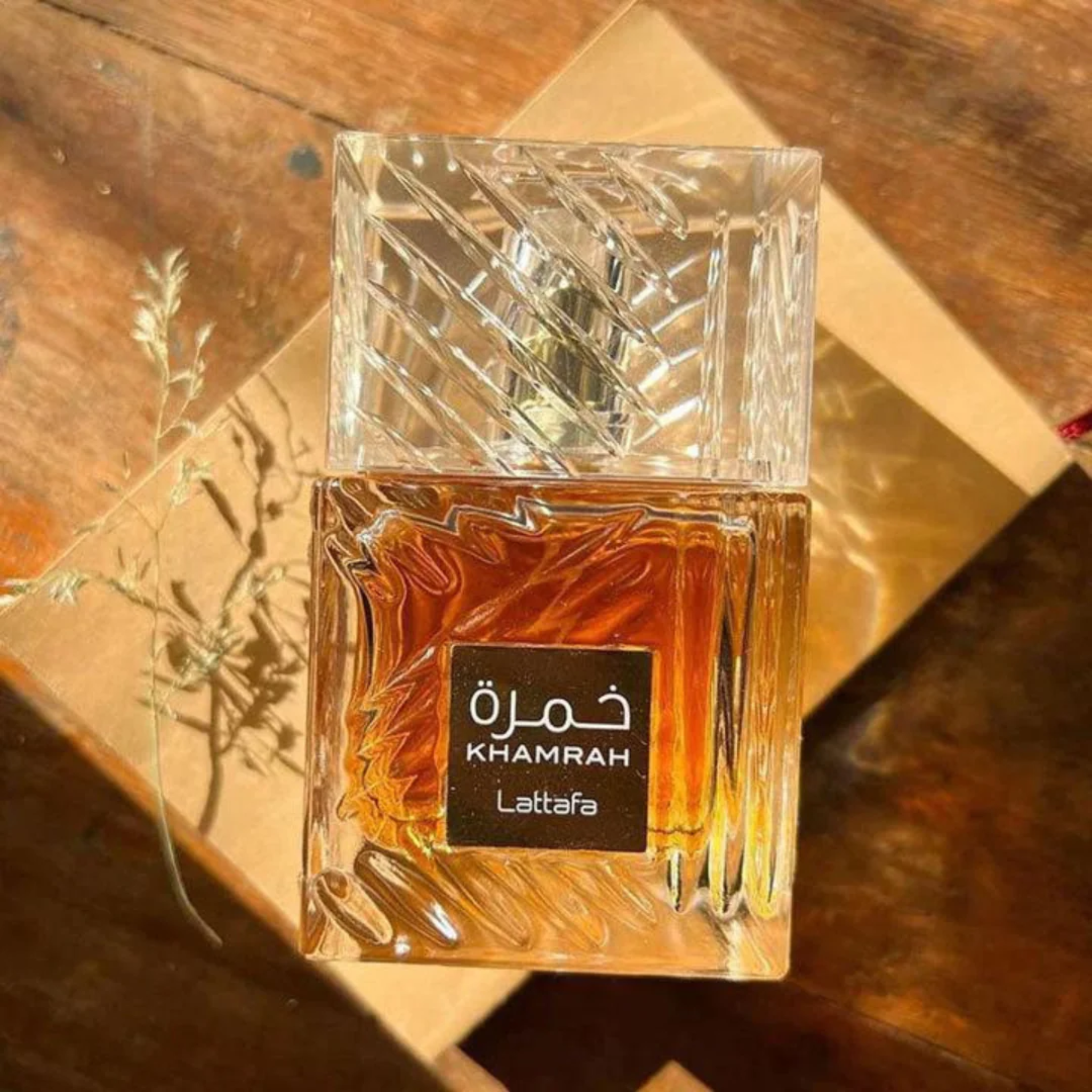 Lattafa Khamrah perfume bottle with rich amber liquid placed on warm wooden surface with sunlight shadows creating a luxury aesthetic