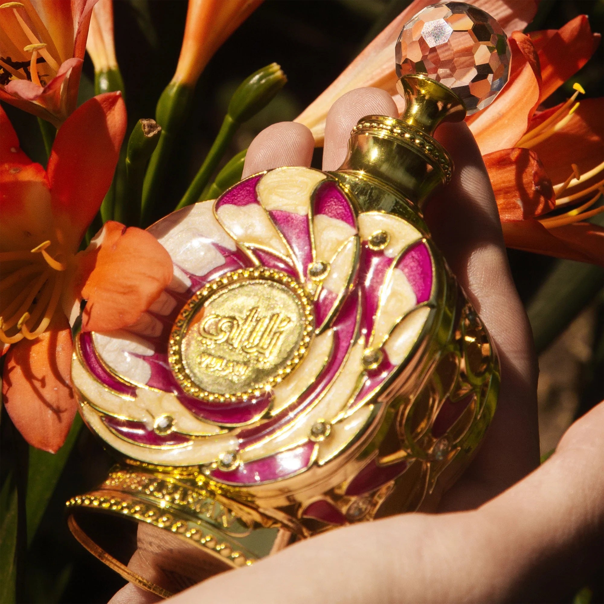 Stunning Yulali perfume bottle by Swiss Arabian held against vibrant orange flowers, showcasing its intricate design and luxury.